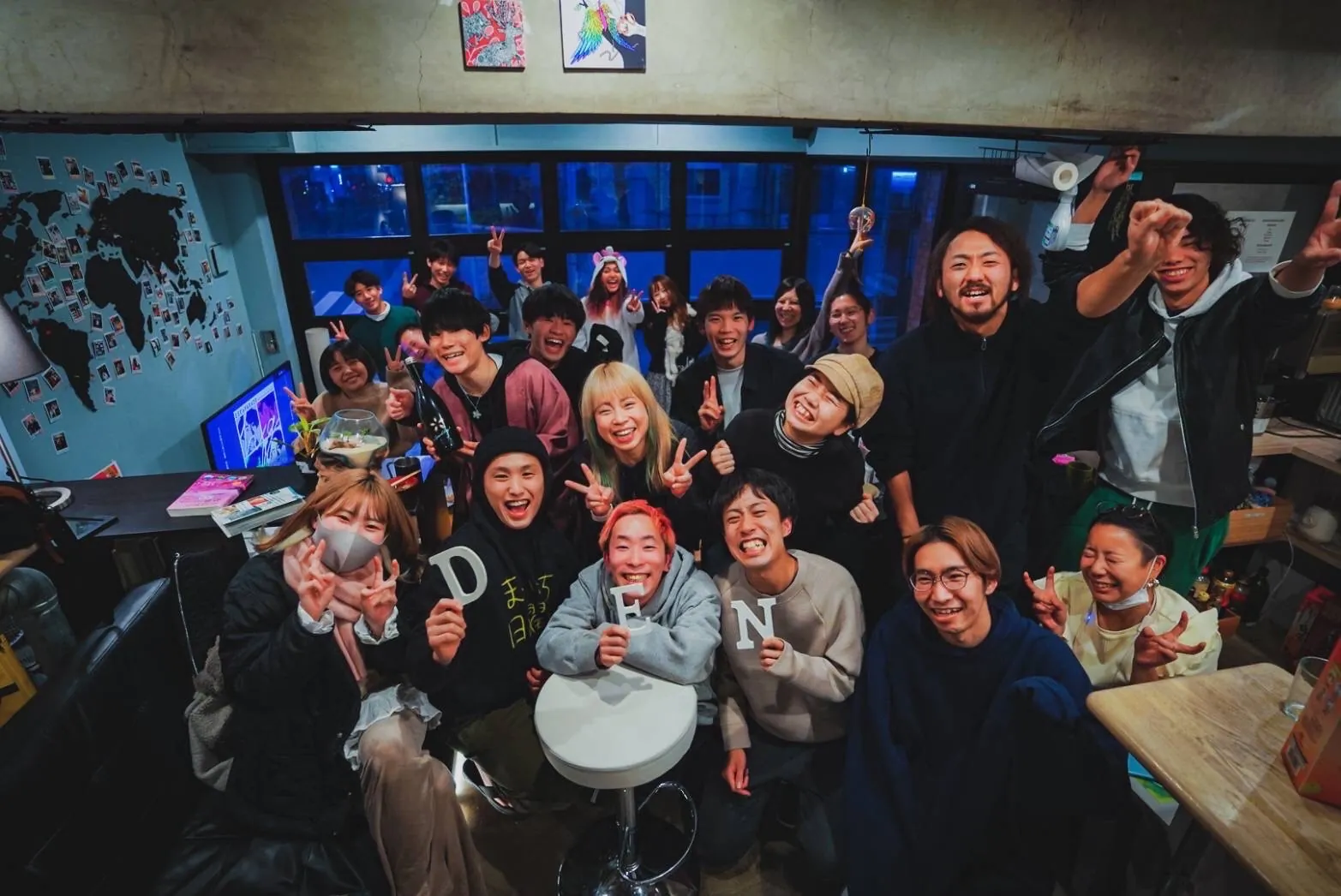 A big group of people gathered in the DEN lounge in front of a world-map wall