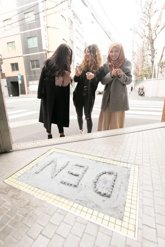 A DEN mosaic set into the pavement, with three people walking past