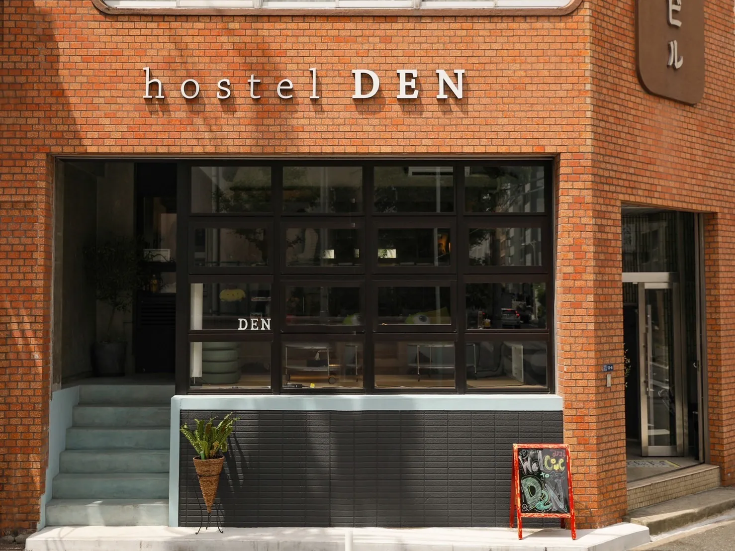 The red-brick building of hostel DEN by day, with the hostel DEN sign above a large black-framed window