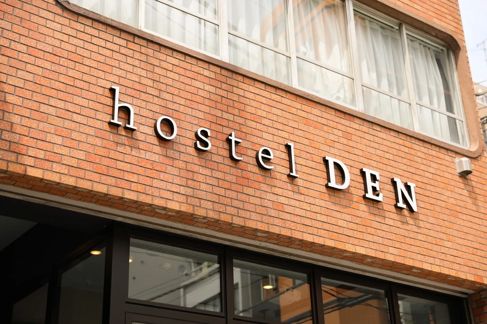 The hostel DEN sign in silver letters on the red-brick wall